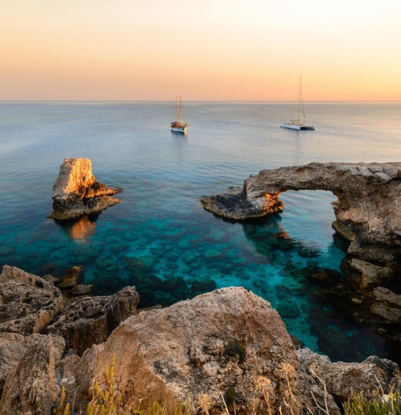 Taken at sunset from a rocky outcrop the camera looks out onto a crystal clear sea and the sea beyond at Famagusta, Northern Cyprus. In the background is a traditional boat next to a modern boat.