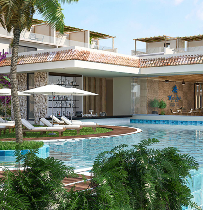A CGI show of a luxury apartment complex poolside in Kyrenia. To the left of the image are sunbeds and parasoles and in the foreground are various dark green plants.